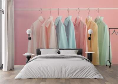 A row of pastel colored shirts on hangers, creating a soft and minimalistic fashion display with a pink gradient background. Wall mural