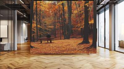 A solitary person sitting on a bench in an autumn forest with orange and yellow leaves, capturing a serene moment in nature. Wall mural