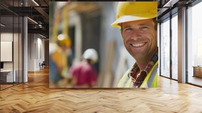 Close-up of a happy construction worker with a yellow hard hat and safety vest, with colleagues working in the background. Wall mural