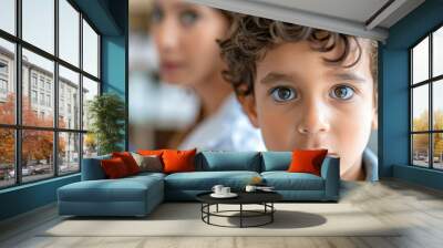 Close-up portrait of a young curly-haired child with an intense gaze, blurred adult figure in the background. Wall mural