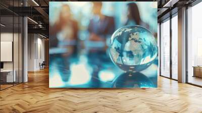 Crystal globe on a reflective office meeting table with blurred silhouettes of businesspeople in the background. Wall mural