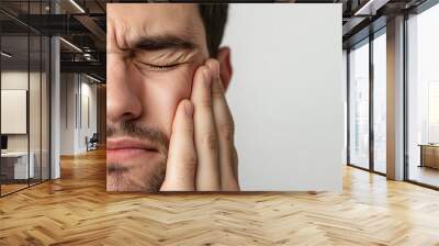 A man closes his eyes and holds his jaw in pain, showing discomfort from toothache or jaw-related pain. His tense expression emphasizes the severity of the discomfort. Wall mural