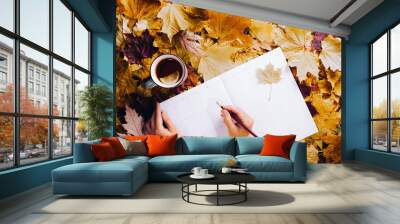 Autumn flat lay - colorful autumn leaves, a cup of tea with lemon, clean week planner, female hands in a yellow hoodie, pencil in hand Wall mural