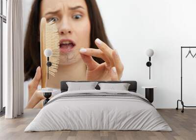 a close horizontal photo of an anxious, sad woman cleaning a comb from accumulated fallen hair and looking at them in panic Wall mural