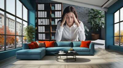 A dejected woman is seated at her office desk, encircled by piles of documents. Wall mural