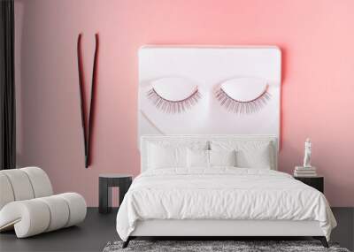 Black false eyelashes and tweezers on a pink background, view from above Wall mural