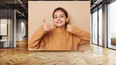 cute girl in sweater posing hand gestures beige background Wall mural