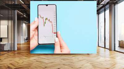 Female hand holding a phone with a stock market graph on blue background. Wall mural