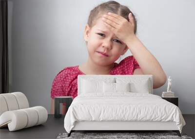 Child with headache holding hand on forehead on white background caucasian little girl 5-6 years in red looking at camera Wall mural