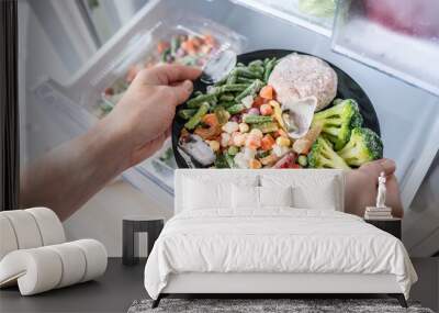 Hands are taking a plate of frozen food out of the freezer of the fridge. Concept of storing ready made food and saving time on cooking dinner Wall mural