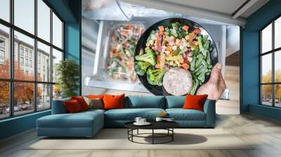 Hands are taking a plate of frozen food out of the freezer of the fridge. Concept of storing ready made food and saving time on cooking dinner Wall mural