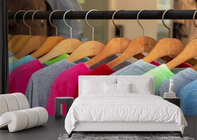 Multicolored shirts and sweatshirts hang on wooden hangers close up. Wall mural