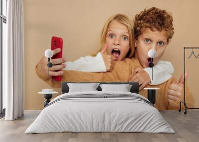 Photo of two children in sweaters posing for fun with phone isolated background Wall mural