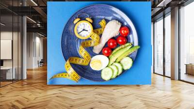 Plate with vegetables and yellow alarm clock on blue background Wall mural