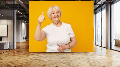 Portrait of an old friendly woman posing face grimace joy yellow background Wall mural