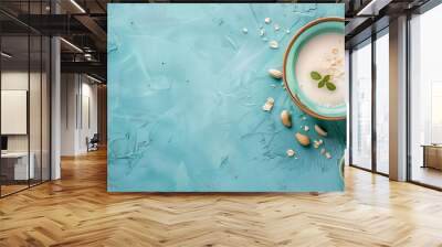 Flat lay of oat milk in turquoise bowl with scattered nuts and oats on a textured cyan background. Ideal for vegan diet, healthy breakfast, and plant-based milk products. Wall mural