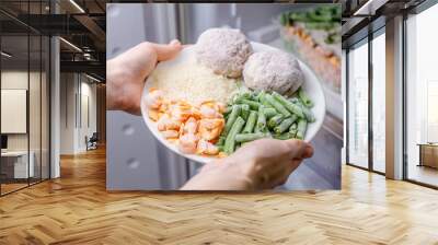 Women's hands are taking a plate of frozen food from the freezer of the fridge. Concept of storing ready made dinner and saving time Wall mural