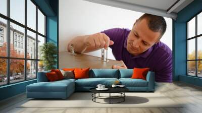 Handsome man assembles furniture in his apartment Wall mural