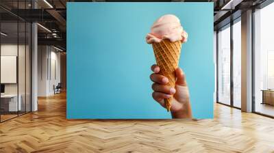 Close up of a childs hand holding a cone with strawberry ice creme scoop, blue background with copy space  Wall mural