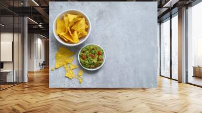 Top view of tortilla chips in a white bowl and avocado guacamole on grey table  Wall mural