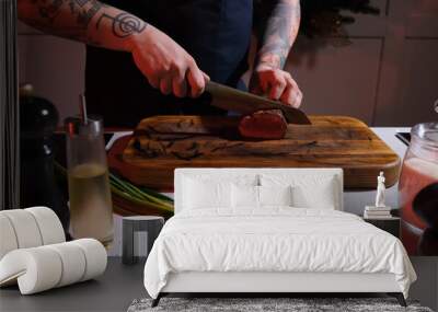 A cook on a wooden board cuts a fried steak into large pieces, close-up Wall mural