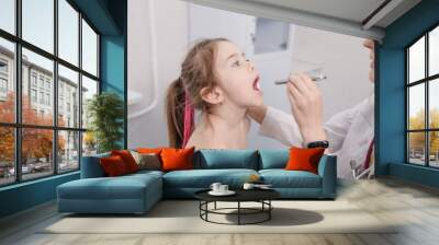 a female doctor checking a little girl's throat with a special flashlight. Wall mural