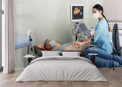 A young girl doctor makes an examination of the abdominal cavity on an ultrasound machine in a male patient. Wall mural