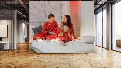 Father mom and two little daughters in bed Happy family in red Christmas pajamas in the bedroom on Christmas morning. new year Wall mural