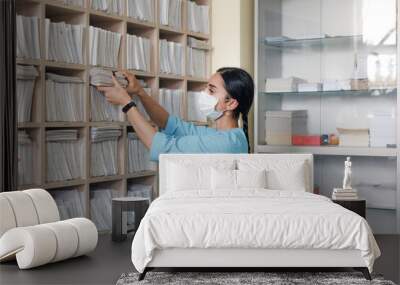 The girl administrator of the medical clinic finds the necessary patient card in the drawer of the rack and checks the correspondence of the last name. Wall mural