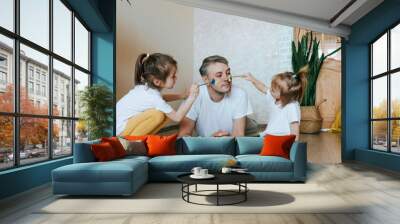 two little girls paint on dad's face with paint Wall mural