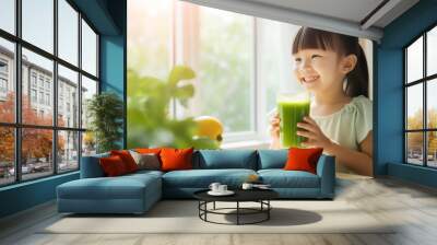 Little kid girl of asian appearance holding a glass of green juice, smoothie, children's health in her hands Wall mural