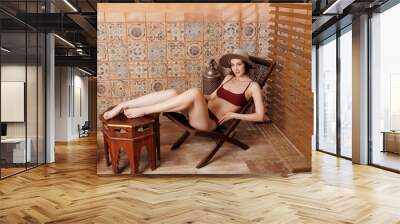 A beautiful slender girl in a brown swimsuit in a Moroccan-style sand studio. A pretty brunette lady with a square hairstyle with lush breasts and slender long legs. A young girl  Wall mural