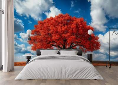 A vibrant red tree stands tall against a blue sky filled with fluffy clouds, showcasing nature’s beautiful colors in autumn. Wall mural