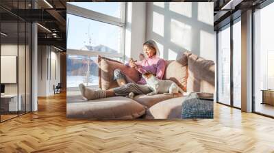 Girl lying on sofa holding phone in her hands in an white sweater on sofa Wall mural