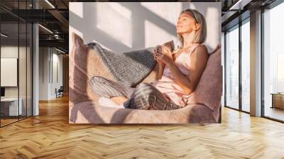 Happy dreamy middle aged woman sitting on sofa in living room with cup of tea or coffee Wall mural