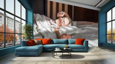 Happy middle aged woman sits on bed and stretching arms Wall mural