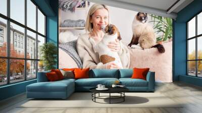 Happy woman playing with her dog on the couch at home Wall mural