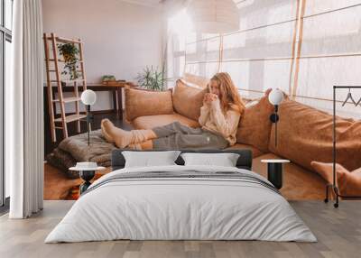 Happy woman relaxing on sofa at home on bright winter morning Wall mural