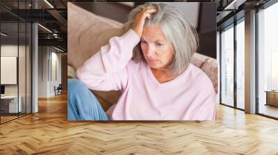 Sad pensive middle age woman looking down depressed sitting on the sofa Wall mural