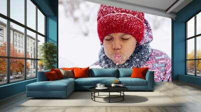 Happy little African-American girl in a red hat and jumpsuit blowing snow off a spruce branch.Winter, Christmas,Happy New Year,active lifestyle concept. Wall mural