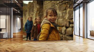 Kids exploring ancient stone ruins wearing colorful jackets. Happy group on an outdoor adventure, discovering history. Smiling children enjoying nature. Wall mural