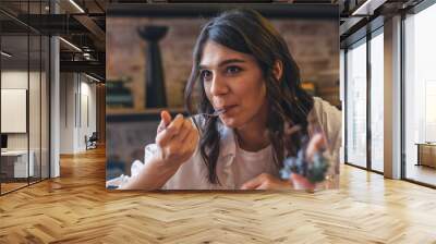 Portrait of a happy young attractive dark-haired woman eating in a cafe. Wall mural