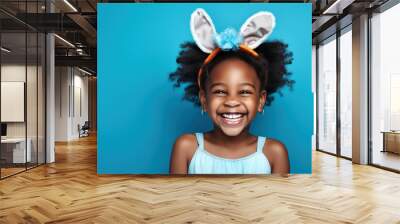 Portrait of an African cheerfully laughing girl with bunny ears on a blue background. Holiday traditions concept. Wall mural
