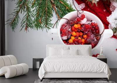 Red scarf, mug with red and orange berries and fir branches on white snow.Christmas, winter, New Year concept. Copy space for text Wall mural