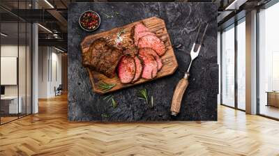 Sliced grilled roast beef with fork for meat on wooden cutting board. Black background. Top view. Wall mural