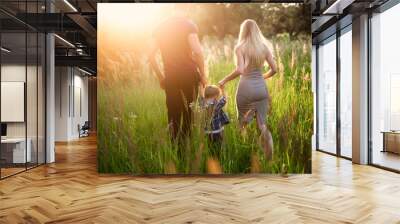 Young healthy parents mom and dad holding his son's hand, embrace and walk together outdoors in sunset light, family, lifestyle, happiness, love, the future Wall mural