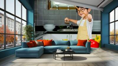 Cute asian little boy  in uniform chef preparing cooking fresh salad in kitchen at home Wall mural