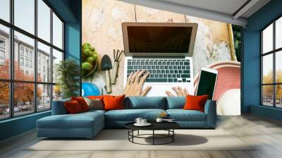 Closeup of hands using laptop to work on table with mobile and gardening accessories. Online marketing. Wall mural