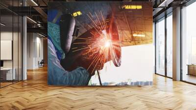 Male worker wearing protective clothing pipe welding with spark light industrial construction fabrication in workshop. Wall mural