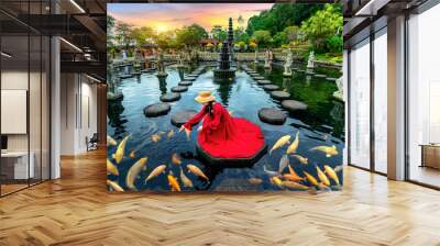 Woman feeding colorful fish in pond at Tirta Gangga Water Palace in Bali, Indonesia. Wall mural